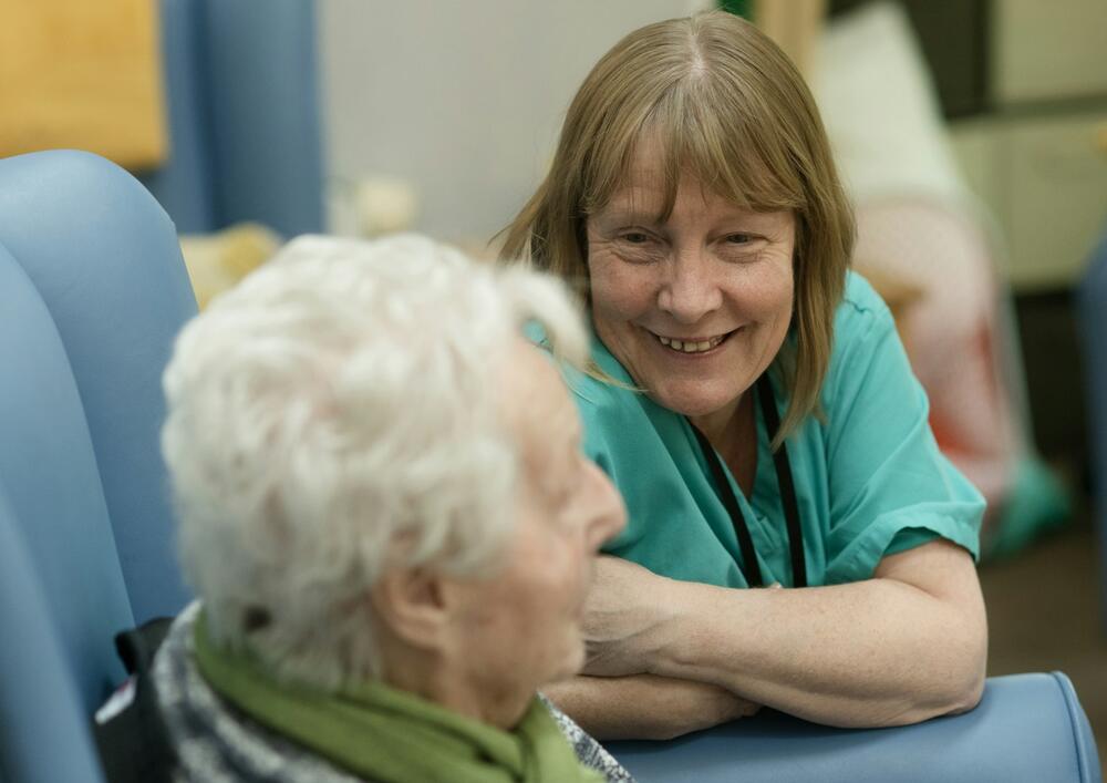 A carer smiling and talking with an elderly resident in an armchair