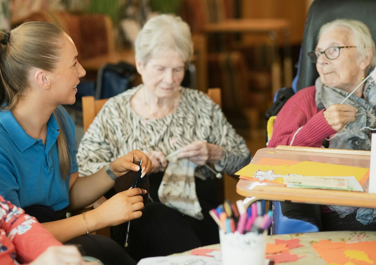 A carer and two residents knitting together in a care home lounge